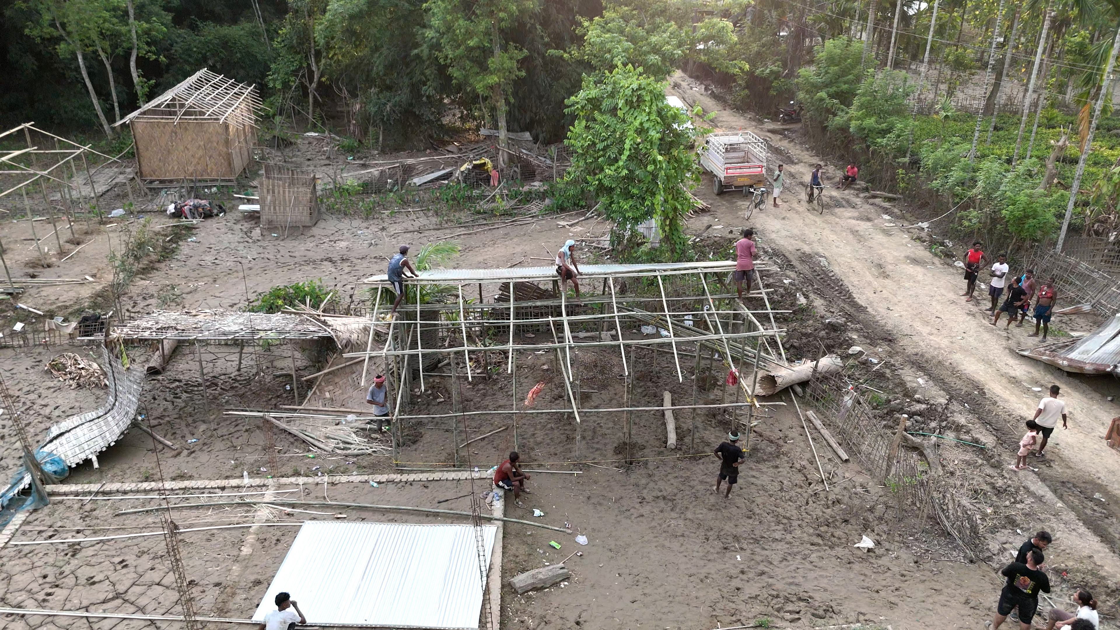 Workers raising a bamboo-framed house on muddy ground in Assam