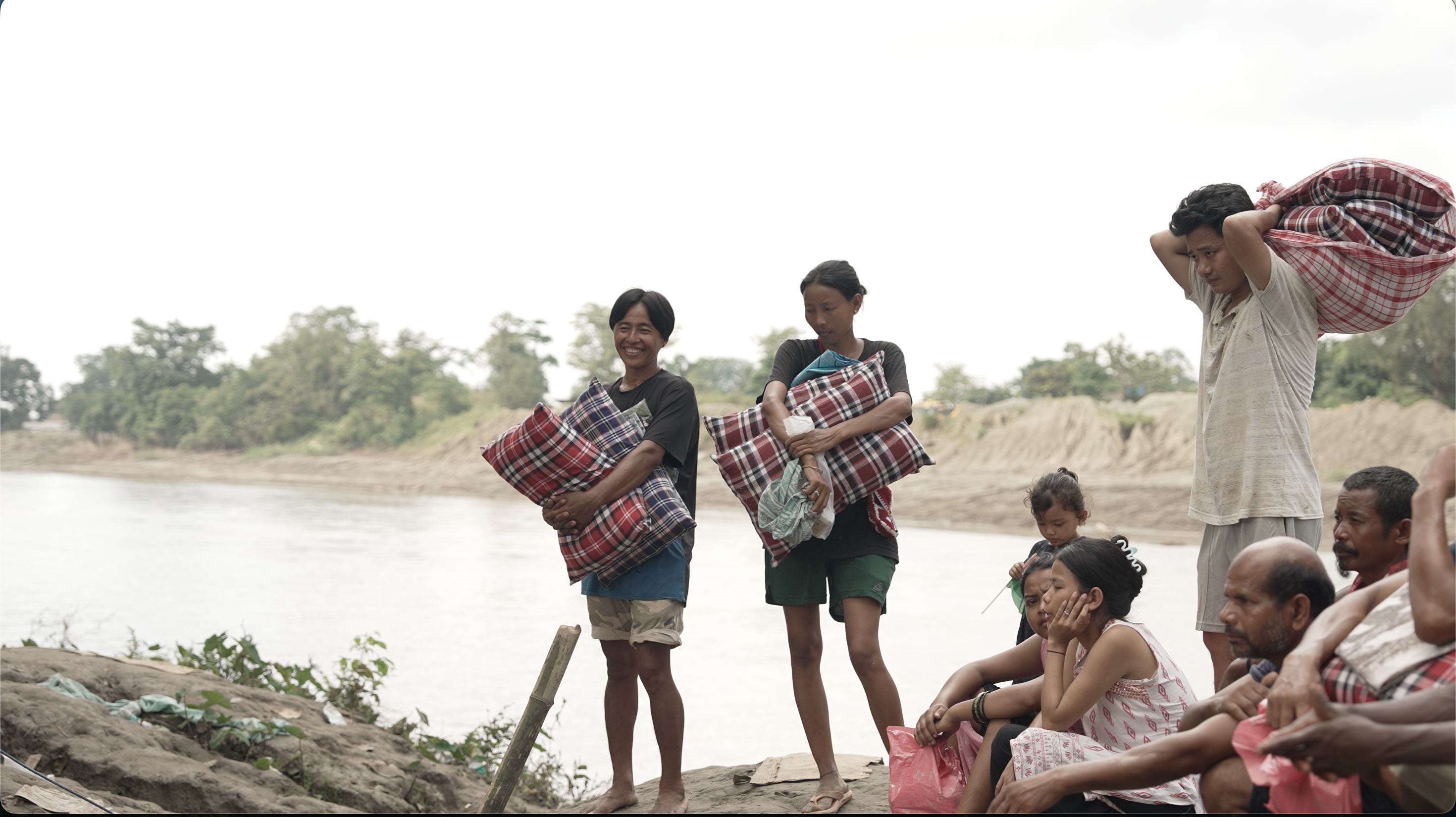 Community members gathered by a river carrying bundles of relief supplies